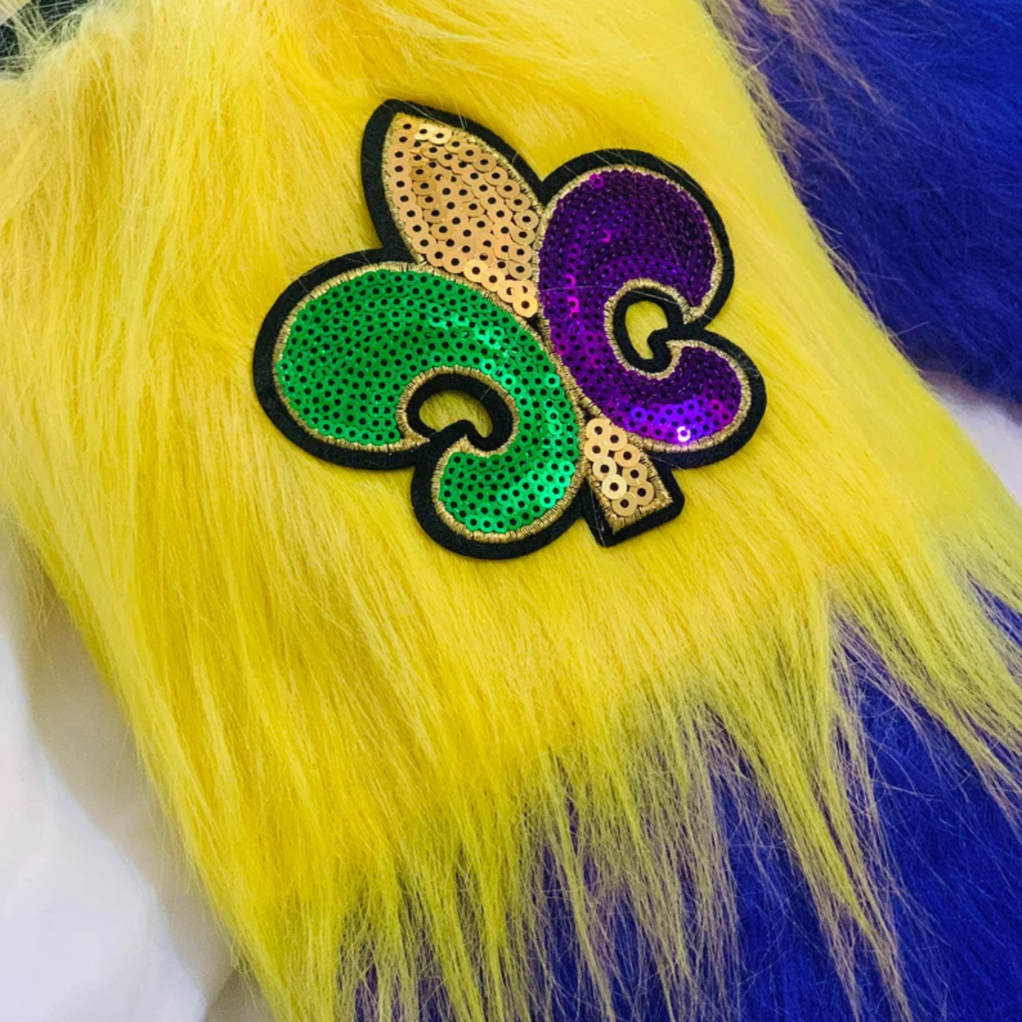 Mardi Gras Furry Leg Warmers with purple, green, and gold stripes, featuring a Fleur-de-Lis patch.